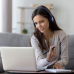 Happy,Young,Woman,In,Headphones,Speaking,Looking,At,Laptop,Making